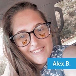 A woman with long brown hair and glasses smiles in a car. She has orange butterfly stickers on her cheeks. She wears a blue floral top. A blue box with white text reads "Alex B.