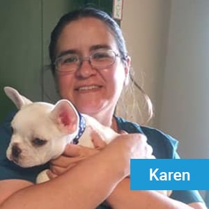 A woman with glasses smiles while holding a small white dog in her arms. The name "Karen" appears in a blue box at the bottom right.