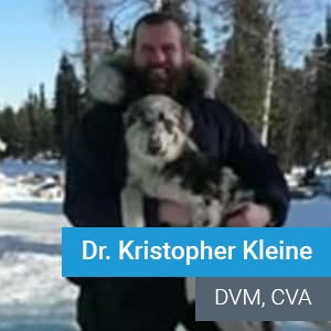 A man in a winter coat holds a dog outside in a snowy landscape with trees in the background. Text on the image reads "Dr. Kristopher Kleine, DVM, CVA.
